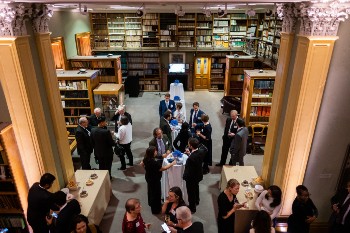 the lower library with shelves of books and people gathered at a party with food and drinks